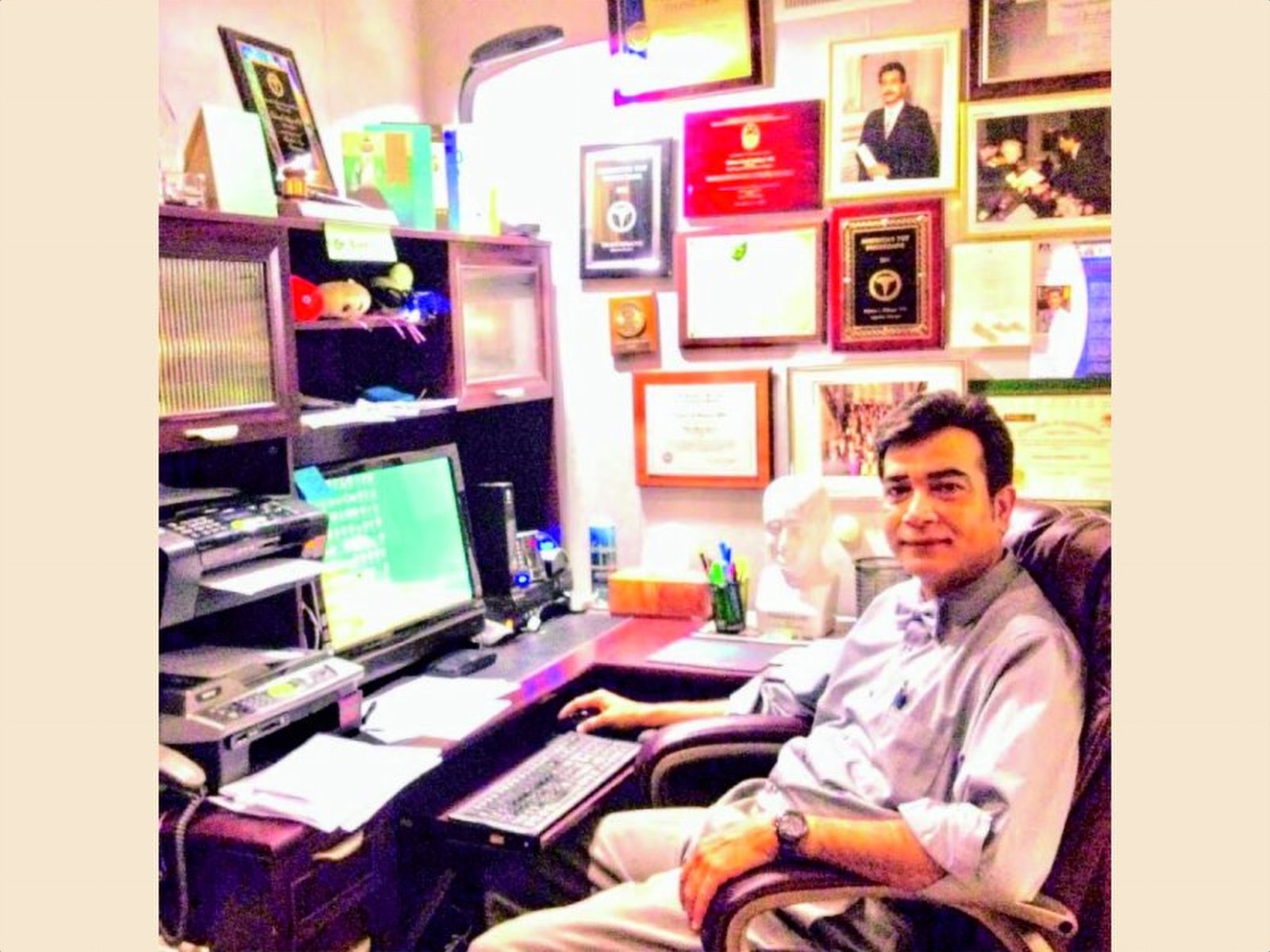 Dr. Siddiqui at his desk before a wall of awards and certifications